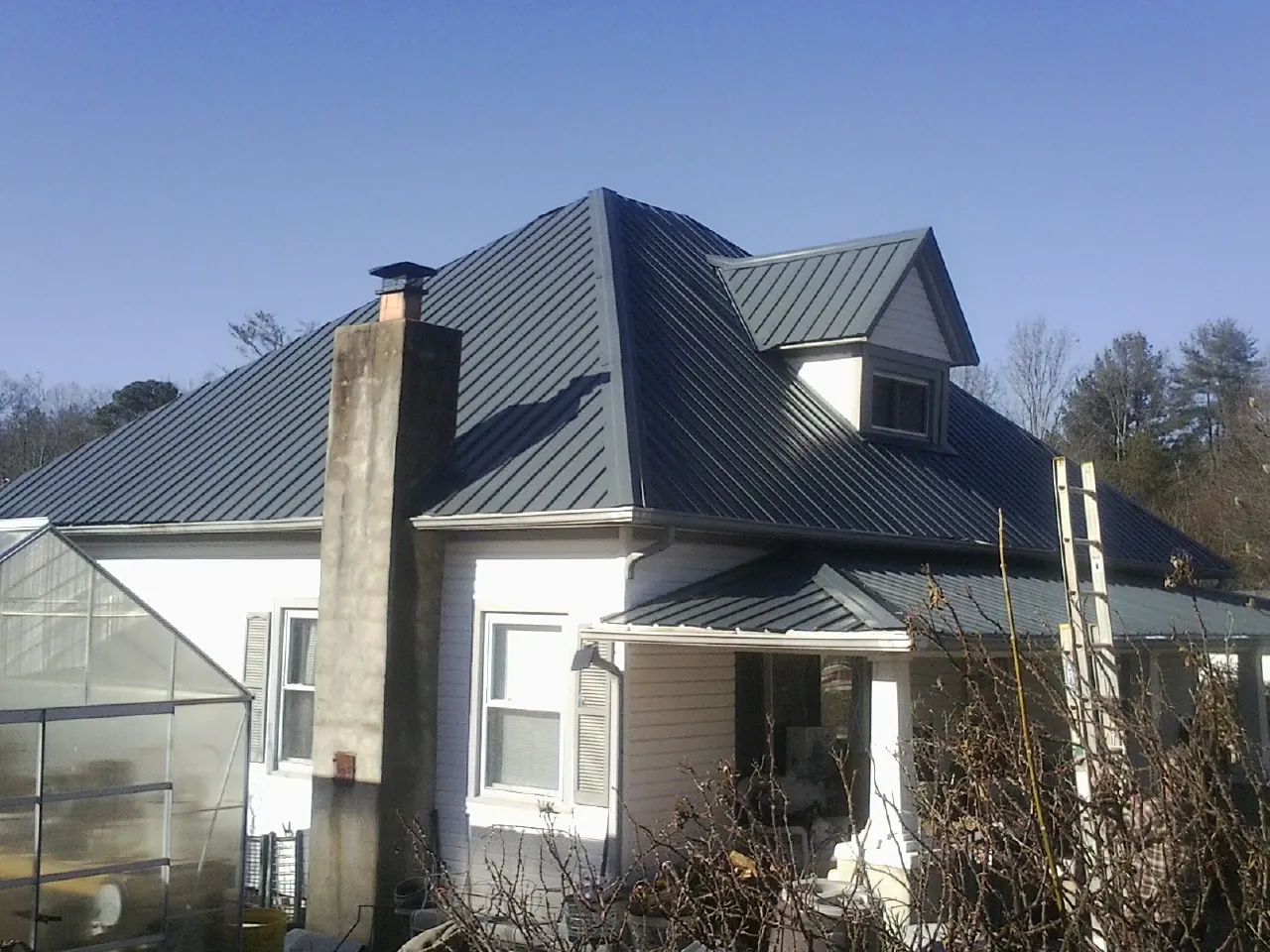 Dark blue standing seam metal roof on a white farmhouse with dormer — Slate & Tile Roof Repair by Roofing Brothers in Lebec