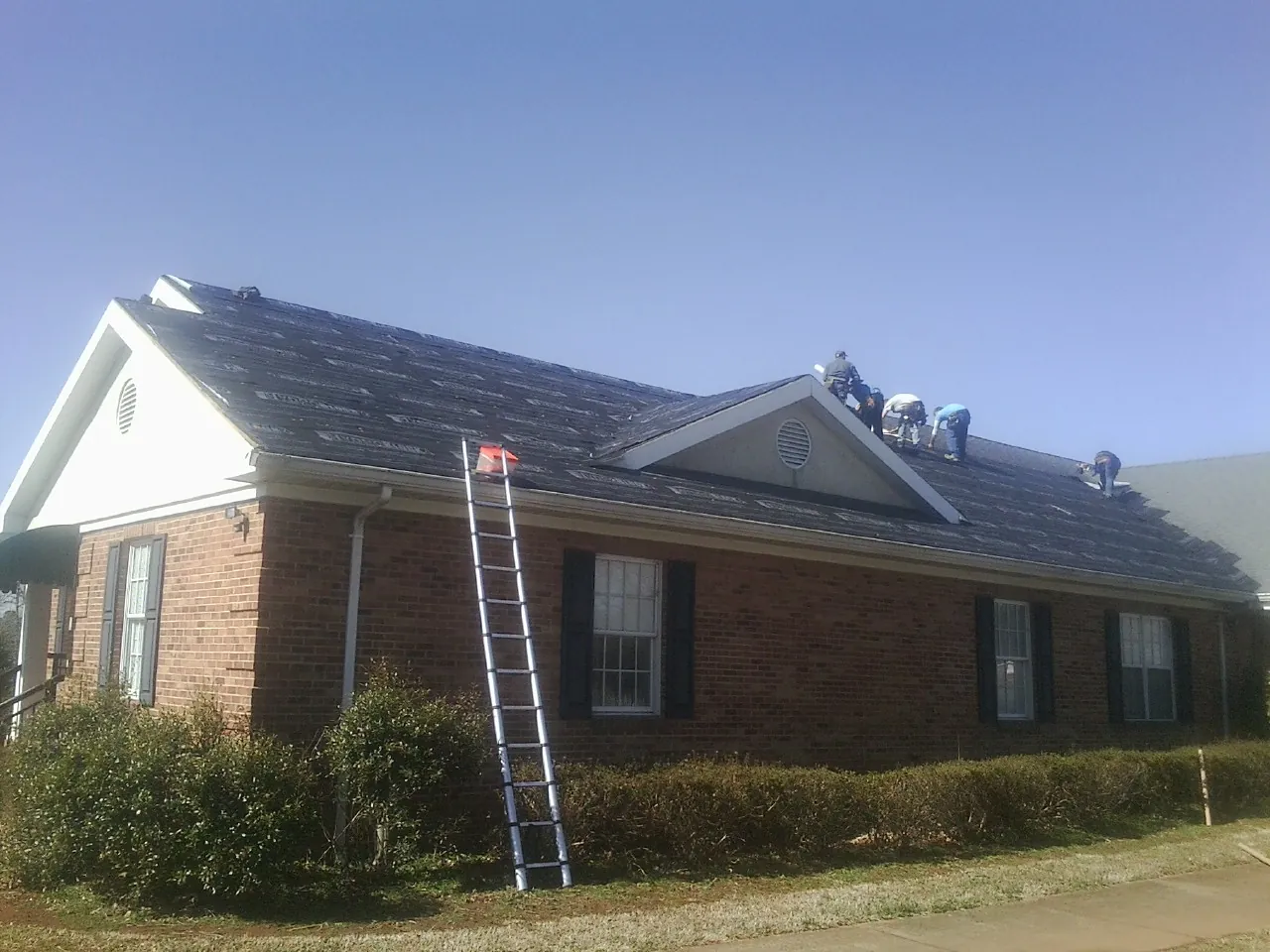 Crew tearing shingles off a brick ranch roof with a ladder set — Emergency Roof Repair work by our crew in Lebec