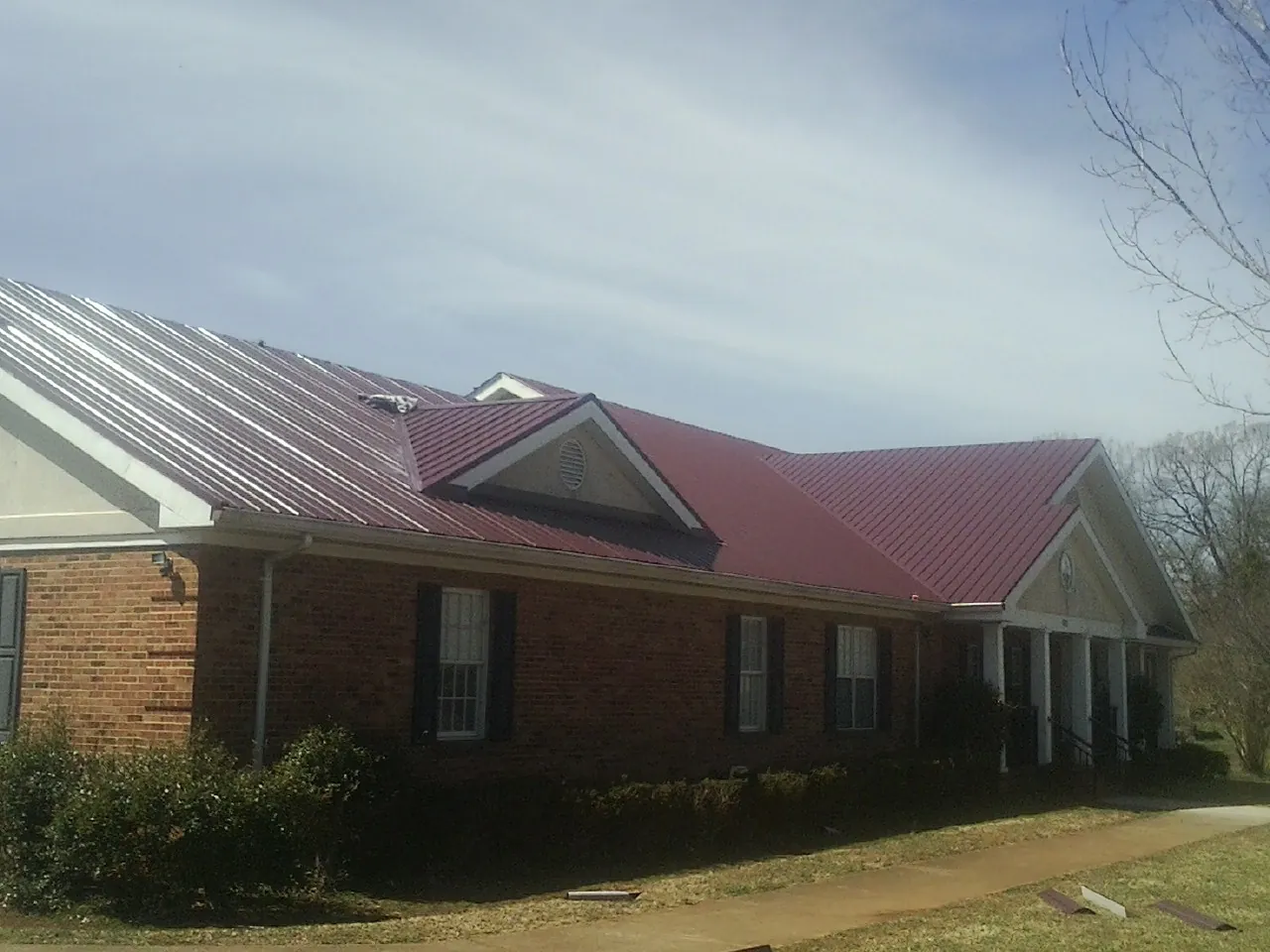 Red metal roof with gabled entries on a long brick building, from a Hail Damage Roof Repair job in Lebec