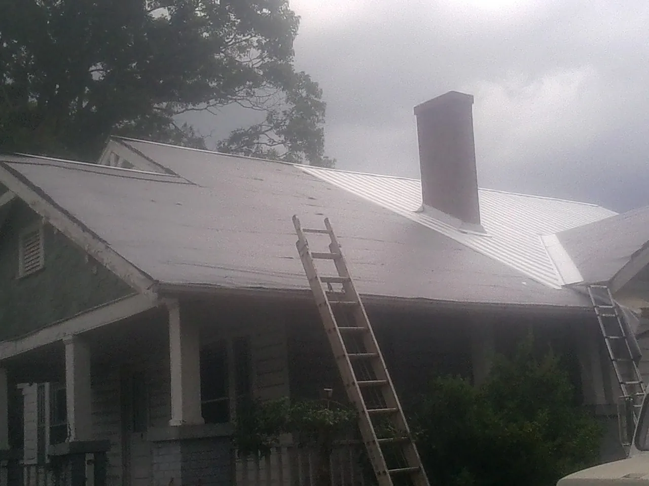 Ladders against a metal roof on an older home with a brick chimney in Lebec