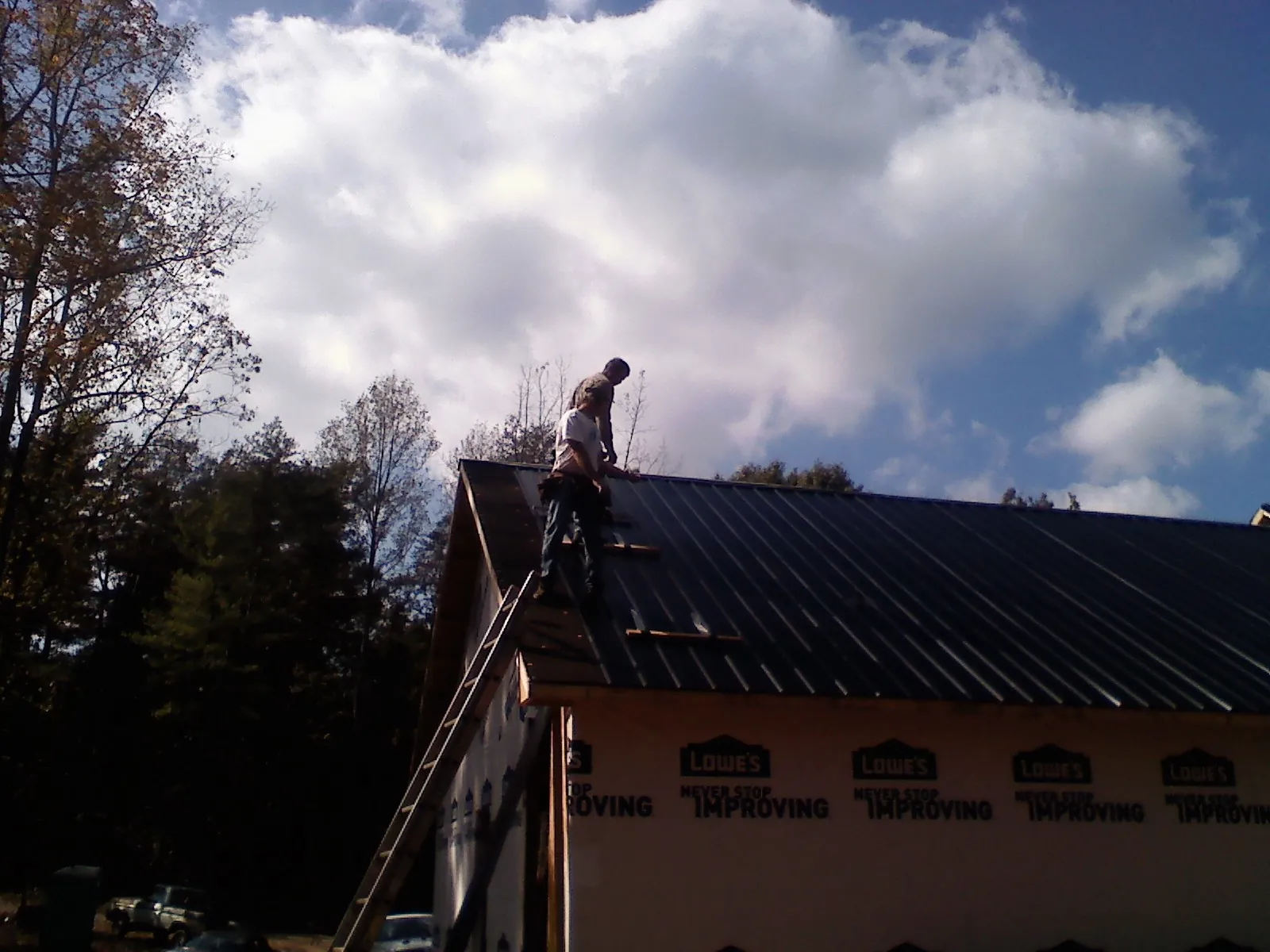 Roofer fastening dark metal panels high against a cloudy sky, from a Roof Inspection job in Lebec